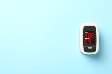 Photo of Modern fingertip pulse oximeter on light blue background, top view. Space for text