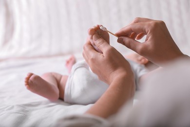 Photo of Mother cleaning baby's foot with cotton bud on bed, closeup