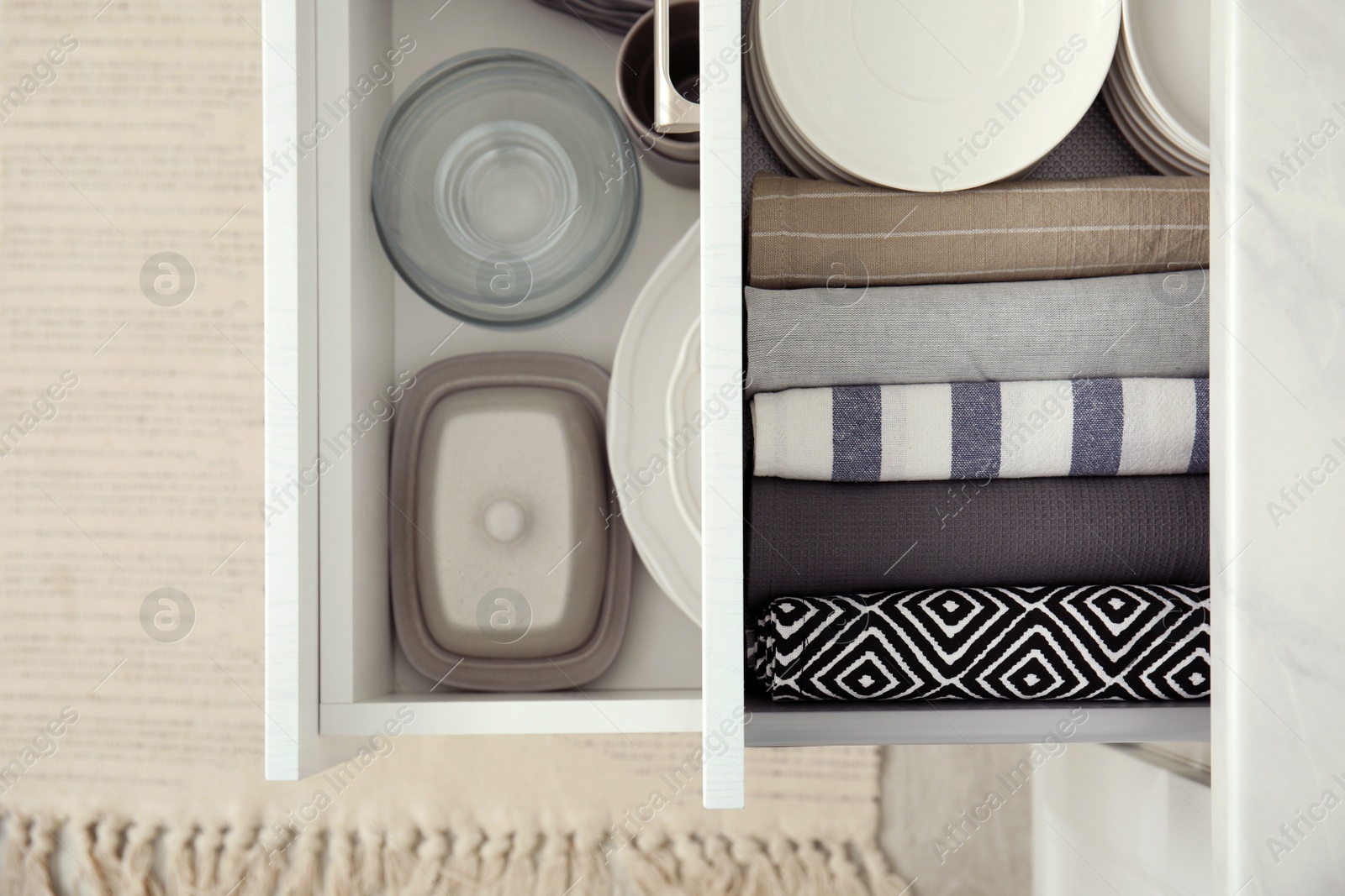 Photo of Open drawers of kitchen cabinet with different dishware and towels, top view