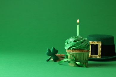Photo of St. Patrick's day party. Tasty cupcake with burning candle and leprechaun hat on green background. Space for text