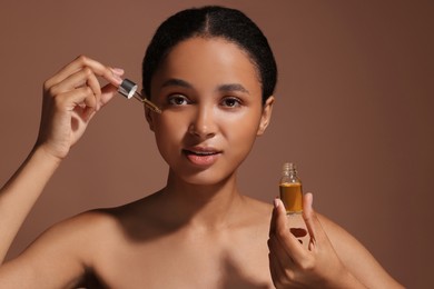Beautiful woman applying serum onto her face on brown background