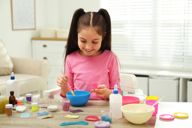 Photo of Cute little girl mixing ingredients with silicone spatula at table. DIY slime toy