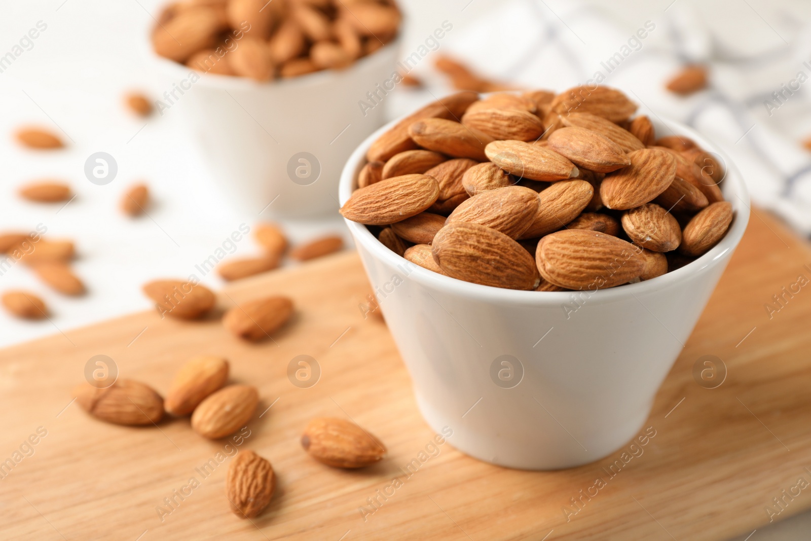 Photo of Tasty organic almond nuts in bowl on wooden board. Space for text