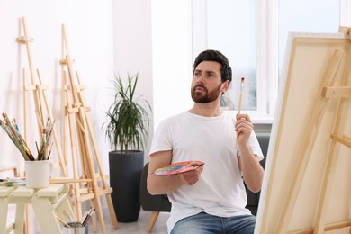 Man painting in studio. Using easel to hold canvas