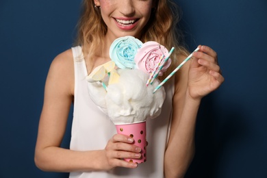 Young woman holding cotton candy dessert on blue background, closeup