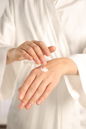 Photo of Woman applying cosmetic cream onto hand, closeup view