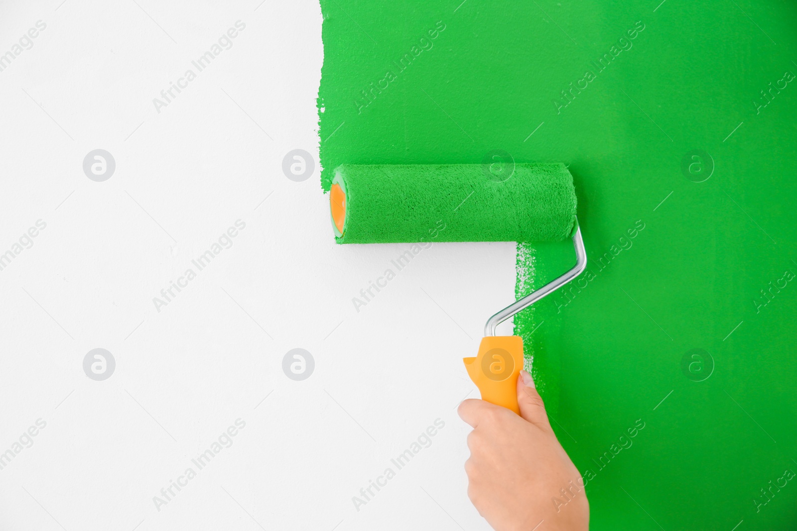 Photo of Woman painting white wall with green dye, closeup. Interior renovation