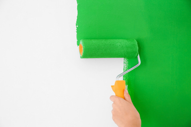 Photo of Woman painting white wall with green dye, closeup. Interior renovation