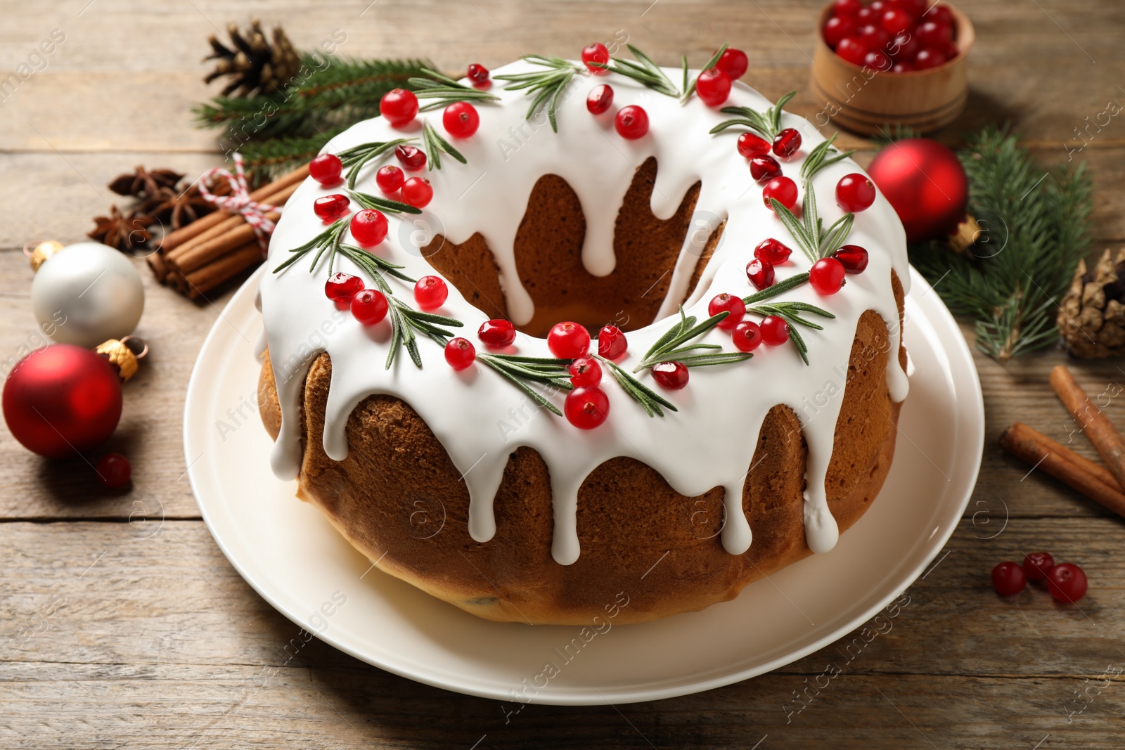 Photo of Traditional Christmas cake with cranberries, pomegranate seeds and rosemary on wooden table