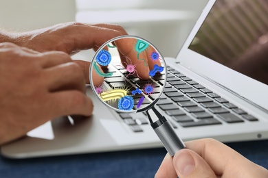 Man with magnifying glass detecting microbes on laptop keyboard, closeup