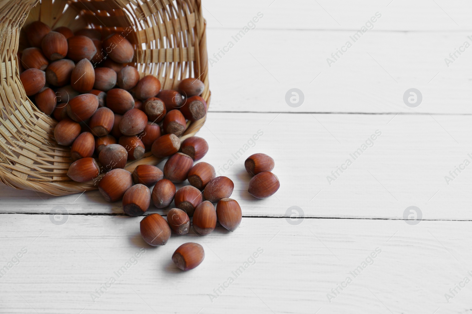 Photo of Hazelnuts with wicker basket on white wooden table. Space for text