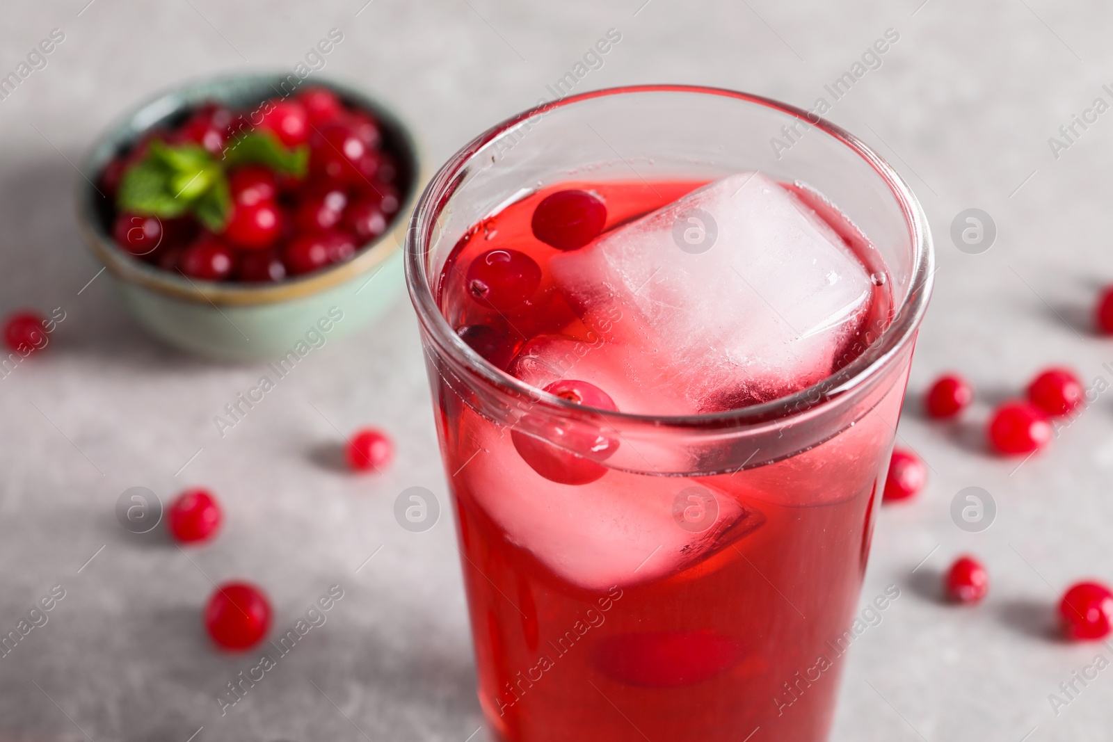 Photo of Tasty cranberry juice with ice cubes in glass and fresh berries on light grey table, closeup