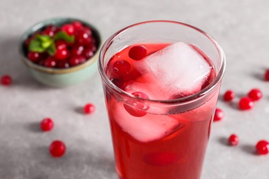 Tasty cranberry juice with ice cubes in glass and fresh berries on light grey table, closeup