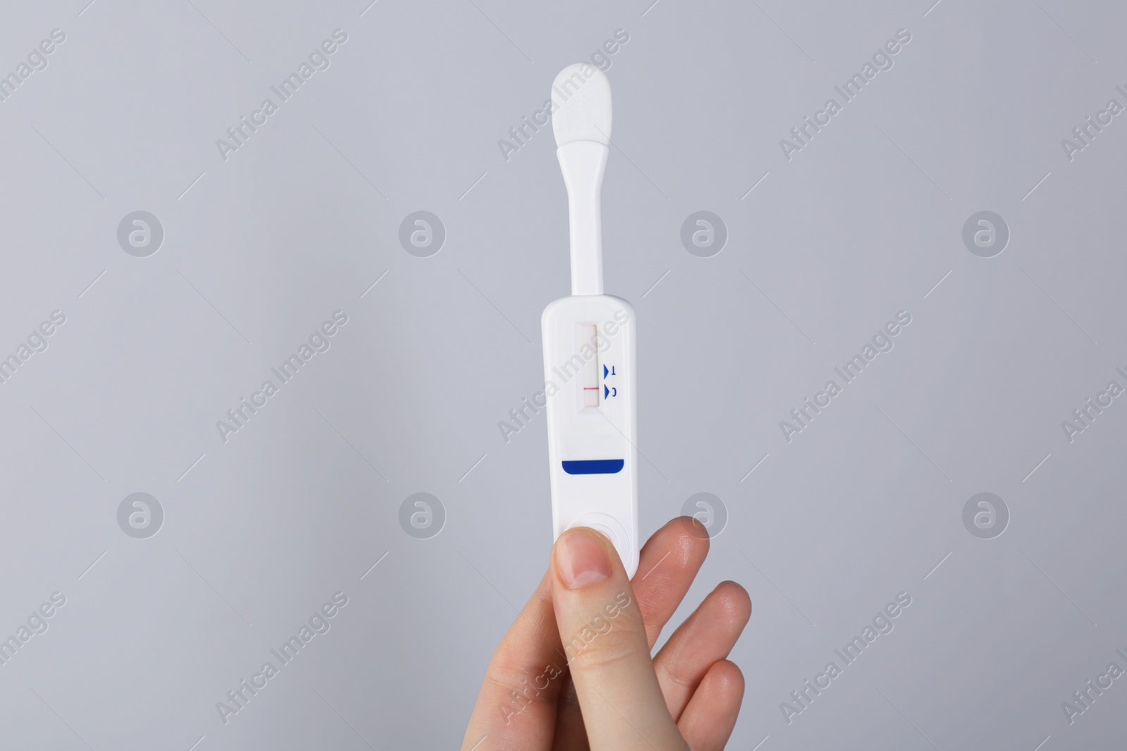 Photo of Woman holding disposable express test on light grey background, closeup