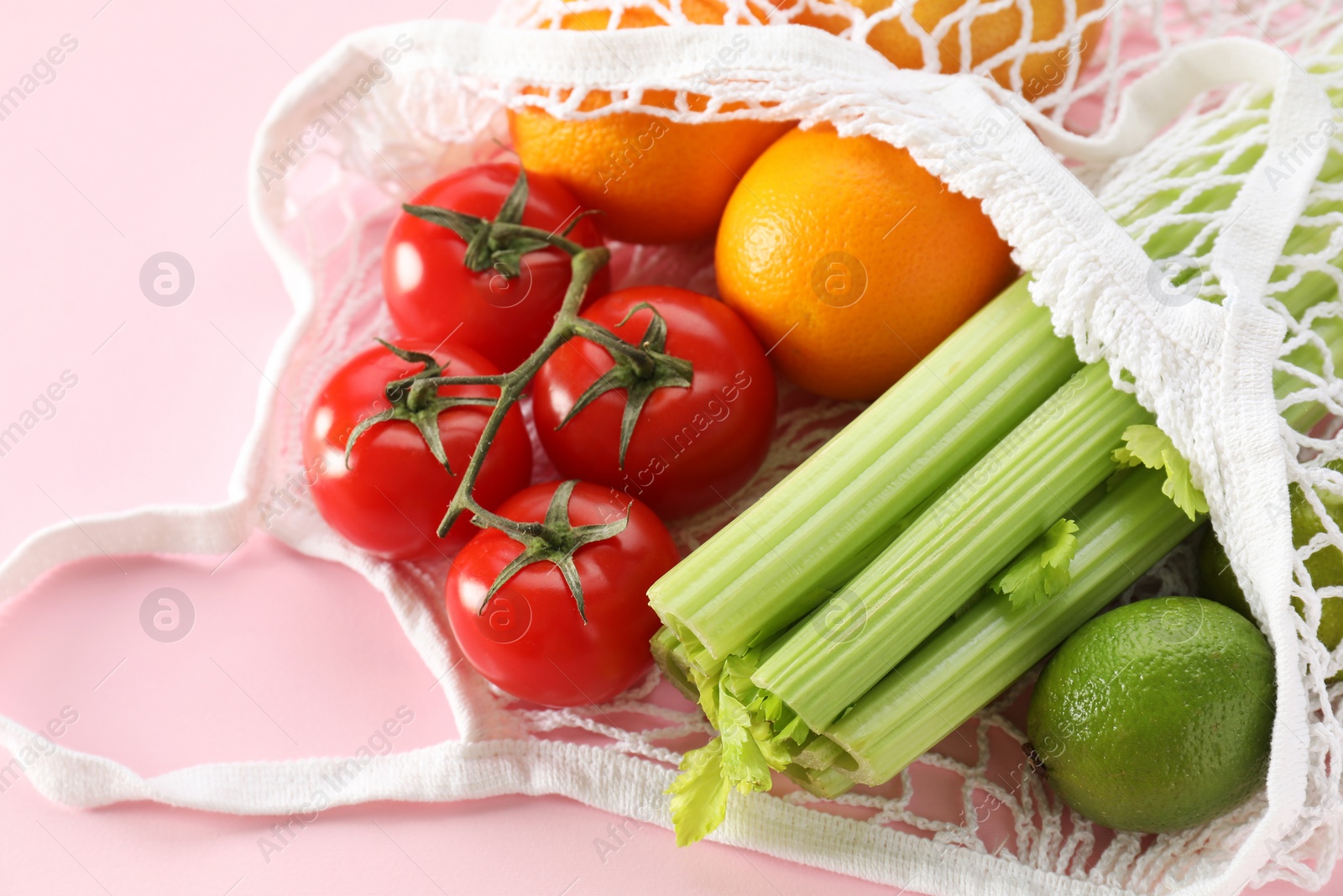 Photo of String bag with different vegetables and fruits on pink background, closeup