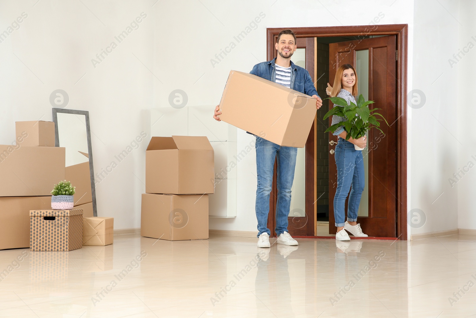 Photo of Couple walking into their new house with moving boxes