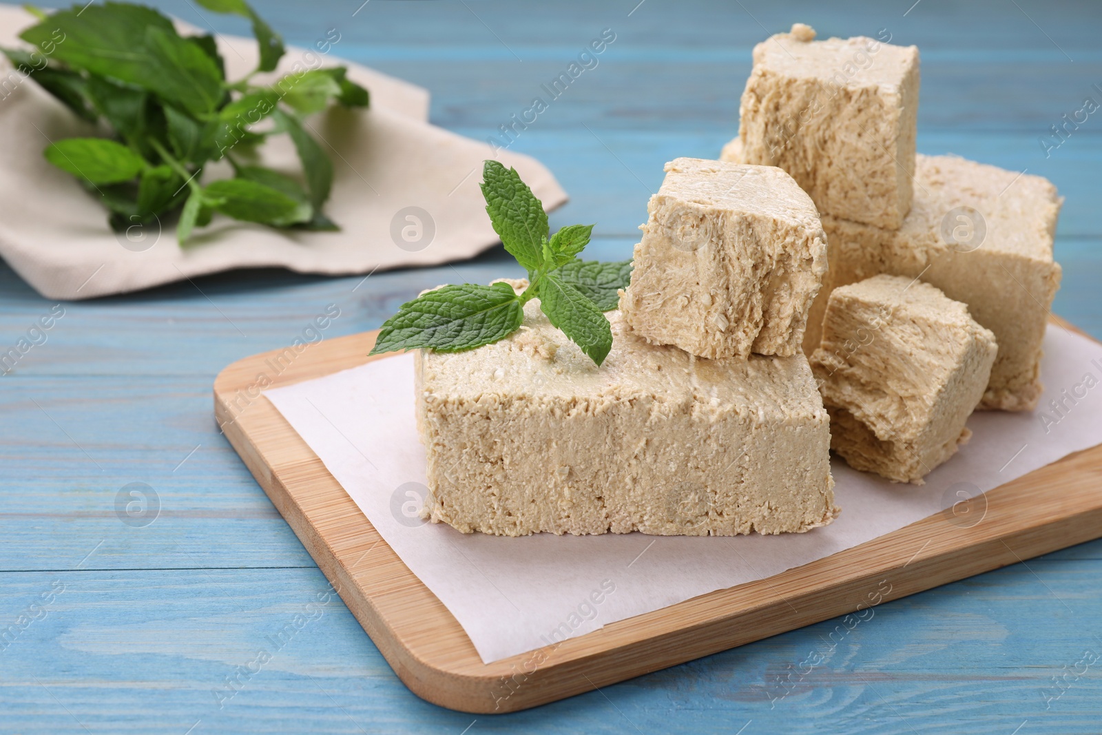 Photo of Pieces of tasty halva and mint on light blue wooden table, closeup. Space for text