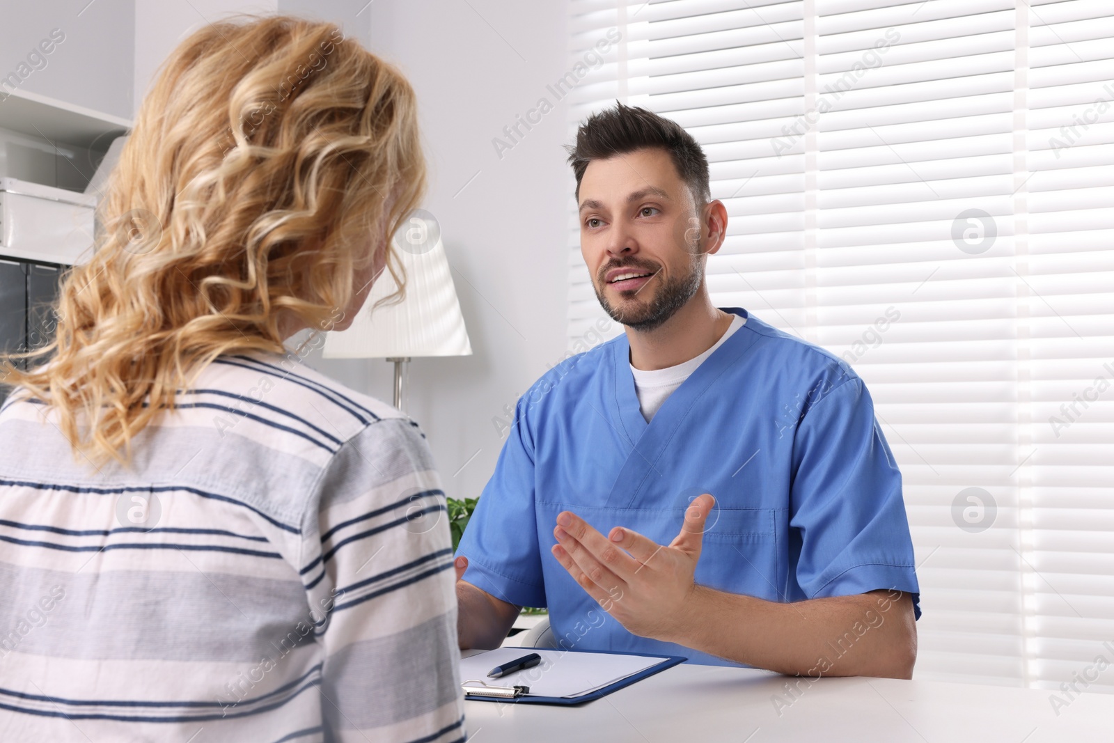 Photo of Doctor with clipboard consulting patient in clinic