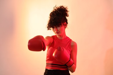 Photo of Beautiful young woman with boxing gloves on color background in neon lights