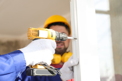 Workers using electric screwdriver for window installation indoors, closeup