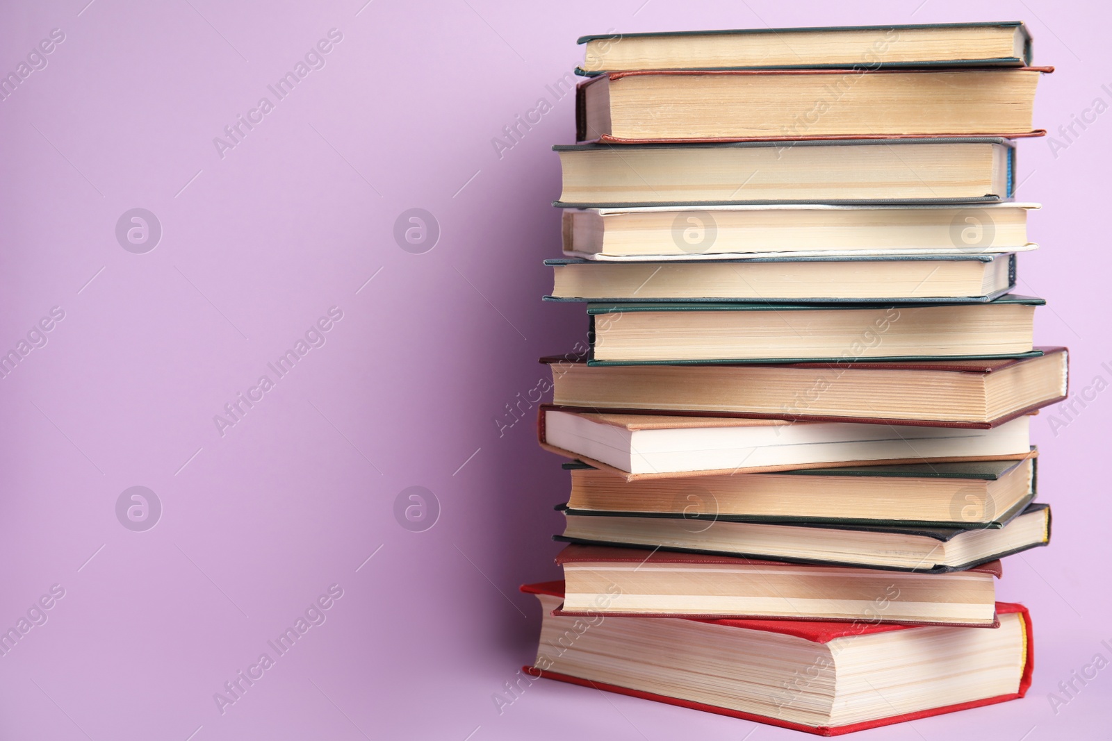 Photo of Stack of hardcover books on violet background. Space for text