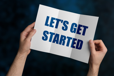 Image of Man holding brochure with phrase LET'S GET STARTED on dark blue background, closeup