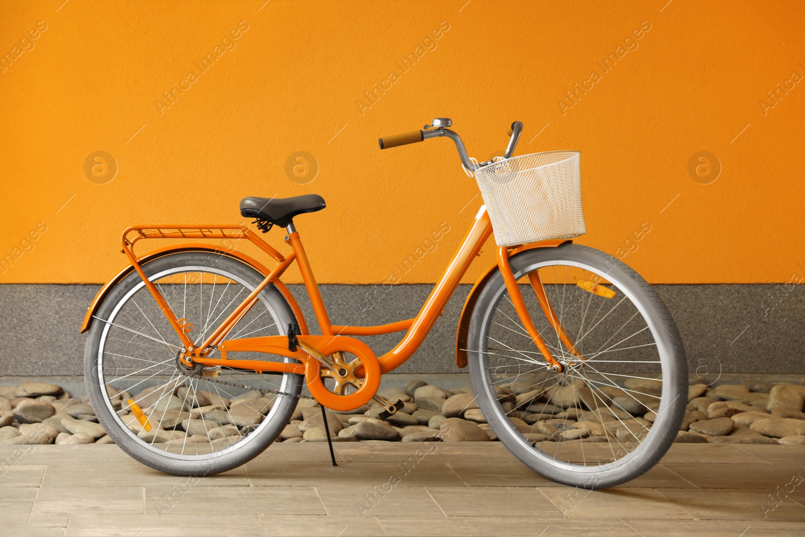 Image of Modern color bicycle with basket near orange wall outside