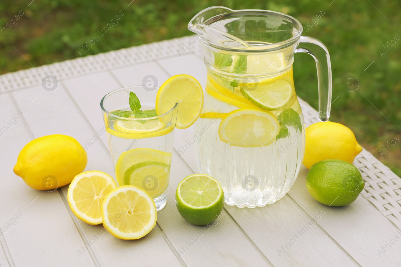 Photo of Water with lemons and limes on white wooden table outdoors