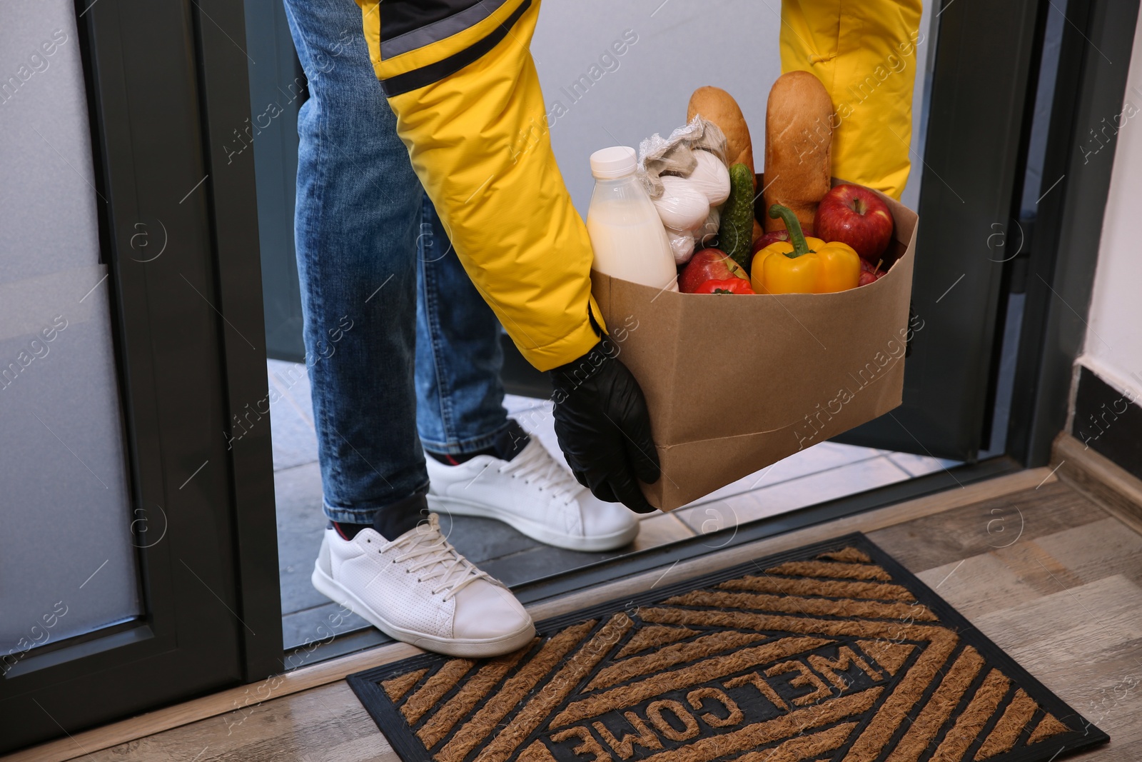 Photo of Courier bring paper bag with food to doorway, closeup. Delivery service during quarantine due Covid-19 outbreak