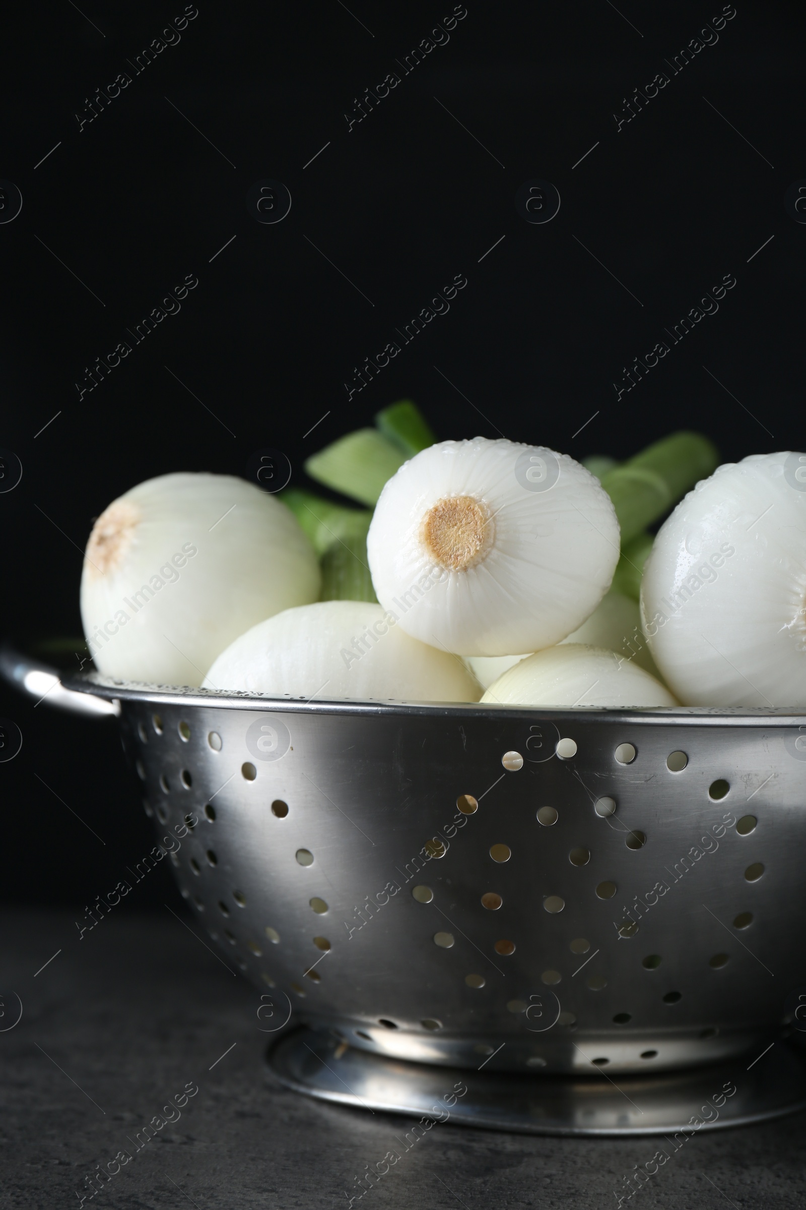 Photo of Colander with green spring onions on black table, closeup