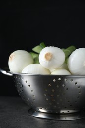 Colander with green spring onions on black table, closeup
