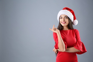 Young beautiful woman in Santa hat on grey background. Christmas celebration