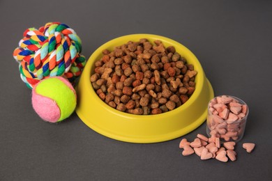 Photo of Vitamins, toys and dry pet food in bowl on grey background