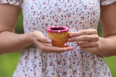 Photo of Woman holding delicious edible biscuit cup of coffee decorated with sprinkles outdoors, closeup