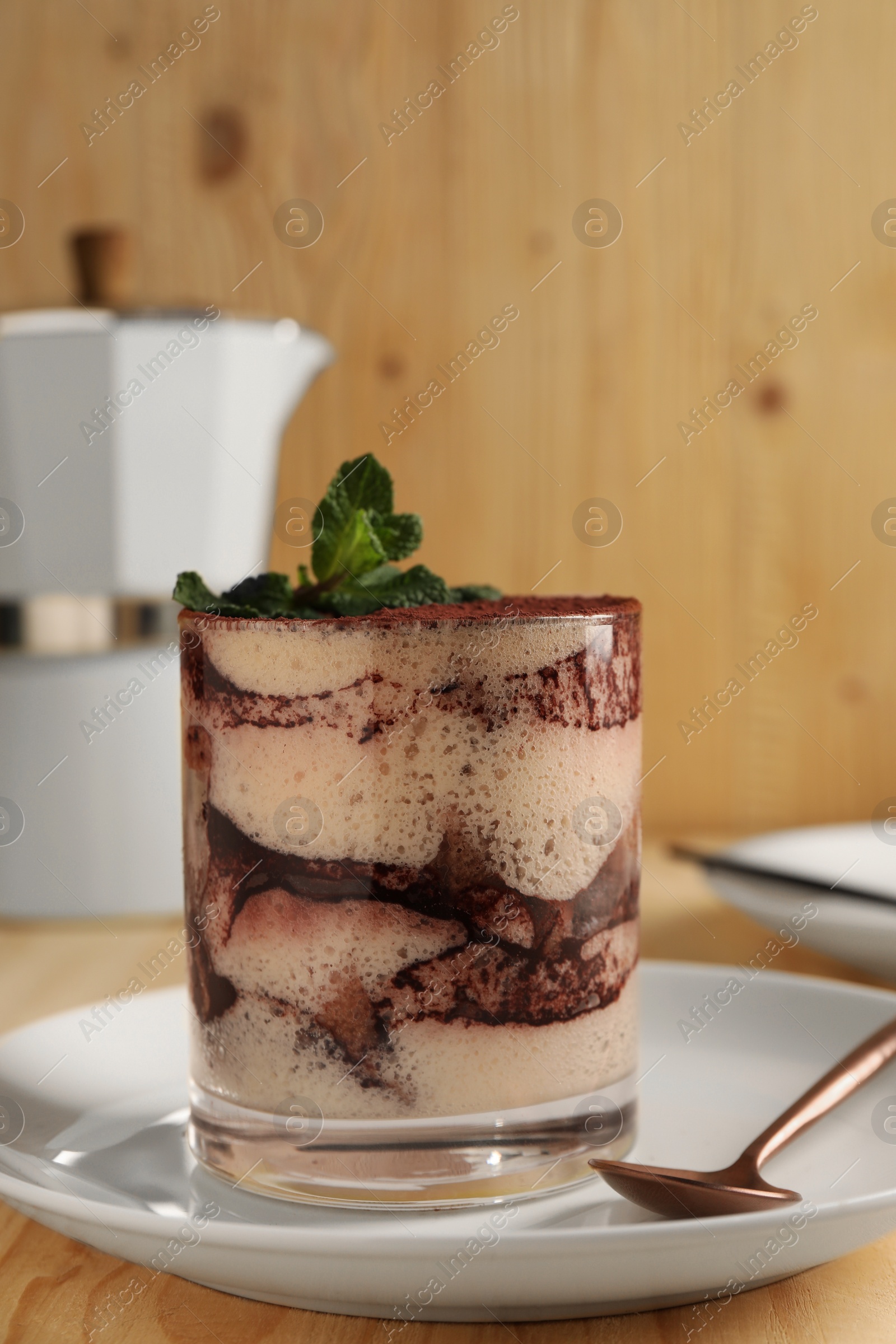 Photo of Tasty tiramisu and mint in glass on light wooden table, closeup