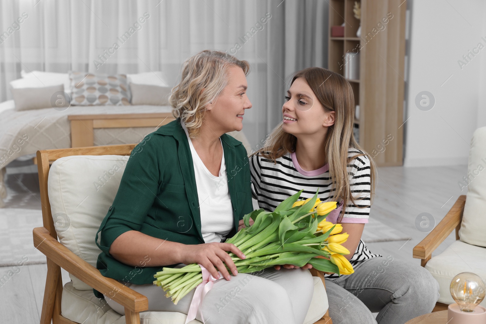 Photo of Young daughter congratulating her mom with flowers at home. Happy Mother's Day