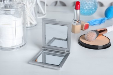 Stylish pocket mirror and cosmetic products on white table
