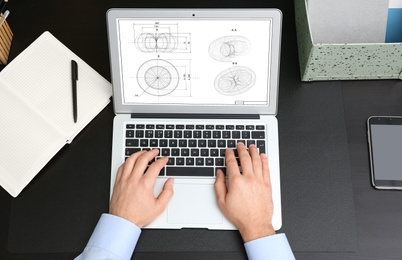 Image of Male engineer working with technical drawing on laptop at table, top view