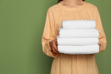 Woman holding folded soft terry towels on green background, closeup. Space for text