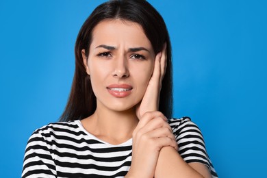 Young woman suffering from ear pain on light blue background