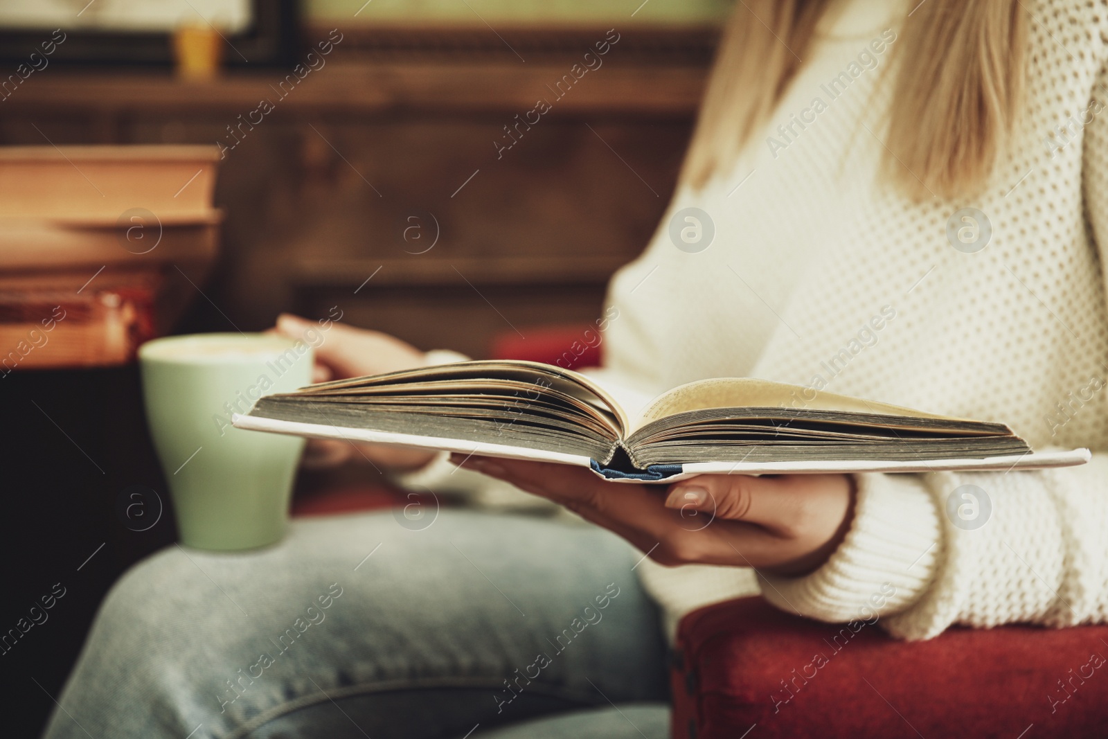 Photo of Woman with cup of coffee reading book indoors, closeup