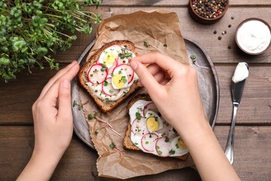 Woman cooking delicious sandwiches with microgreens at wooden table, top view
