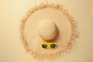 Straw hat and sunglasses on beige background, flat lay. Stylish headdress