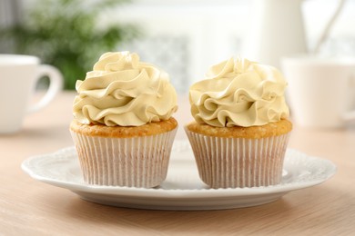 Photo of Tasty cupcakes with vanilla cream on light wooden table, closeup