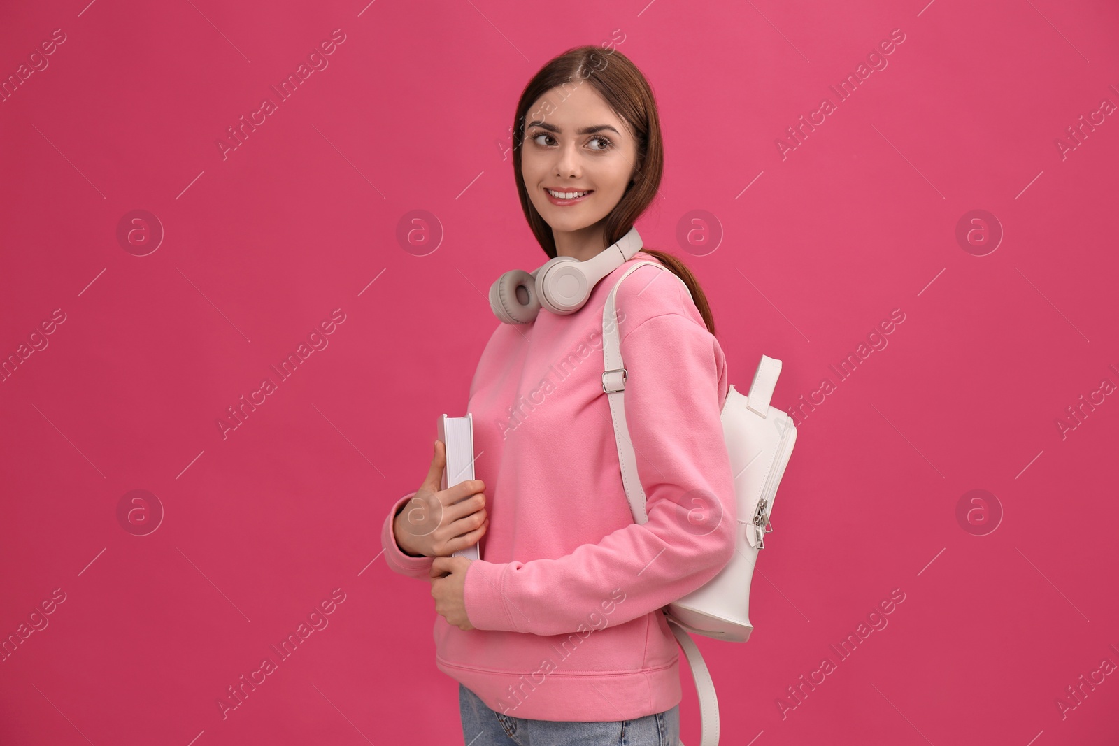 Photo of Teenage student with book, headphones and backpack on pink background