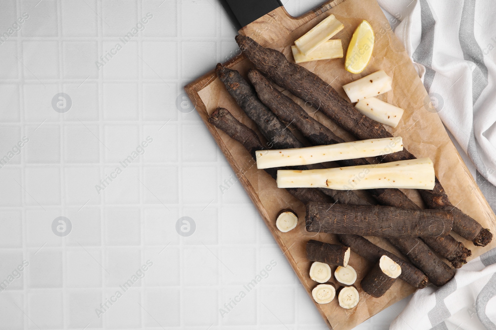 Photo of Raw salsify roots and lemon on white tiled table, top view. Space for text