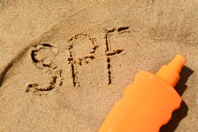 Abbreviation SPF written on sand and blank bottle of sunscreen at beach, top view