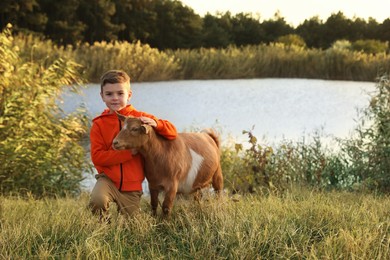 Photo of Farm animal. Cute little boy with goat on pasture near pond, space for text