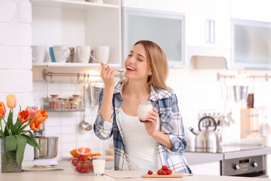 Photo of Young attractive woman eating tasty yogurt at table in kitchen