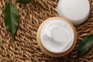 Photo of Jar of face cream and fresh leaves on wicker mat, top view. Space for text